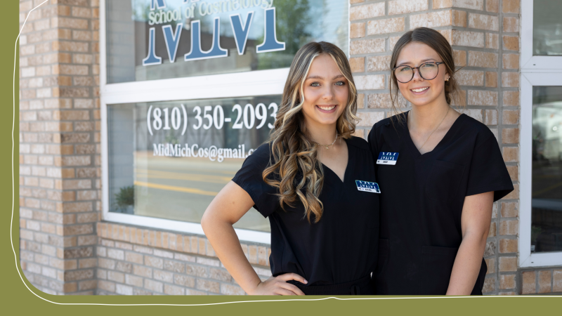Two women stand together posing for a photo in front of a school of cosmetology sign. The woman on the right has long blonde hair and the woman on the left has glasses and has brown hair. They both are wearing school of cosmetology scrubs.