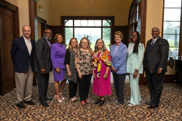 A group of Legacy Society members pose together smiling in an elegant room with tall windows at Warwick Hills Golf Club, 2025.